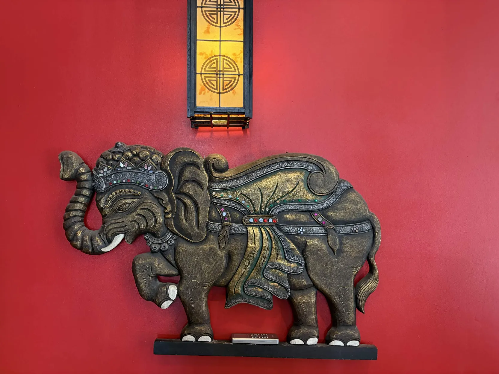 Bas-relief d'éléphant doré sous une lanterne, sur le mur rouge
