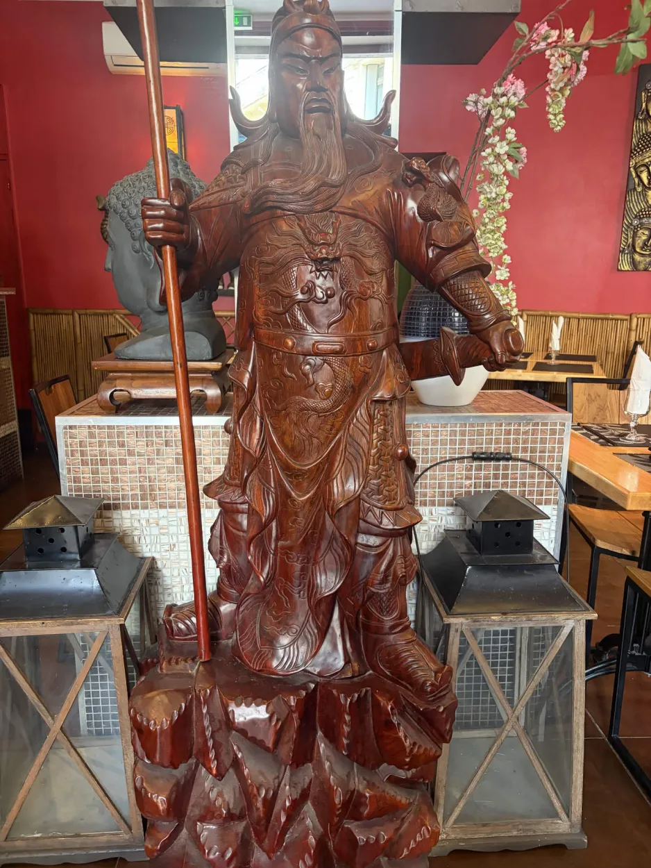 Grande statue de guerrier sculptée en bois entre deux lanternes